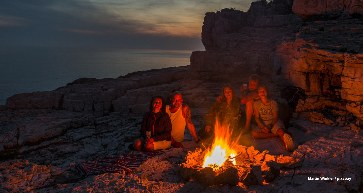 Menschen sitzen auf felsigem Strand am Meer am Lagerfeuer