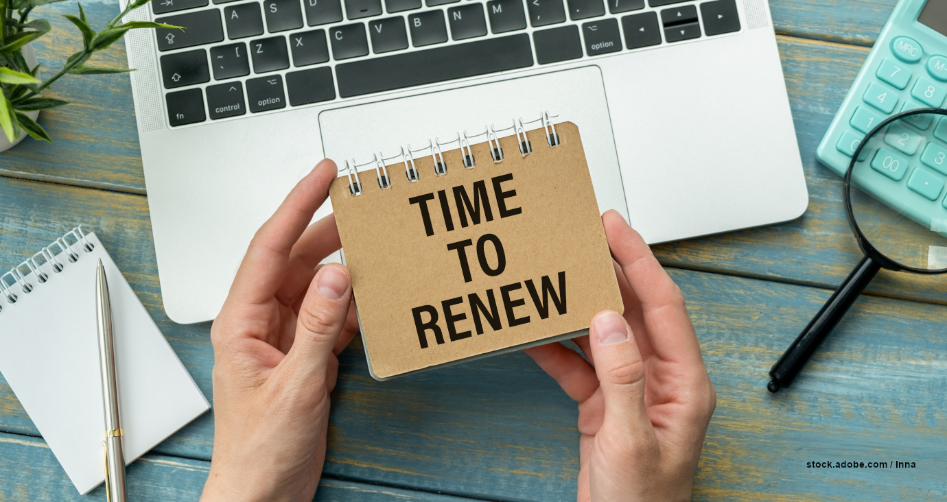 Notiz "Time to Renew" steht auf einem von Händen gehaltenen Block. Ein Laptop im Hintergrund.